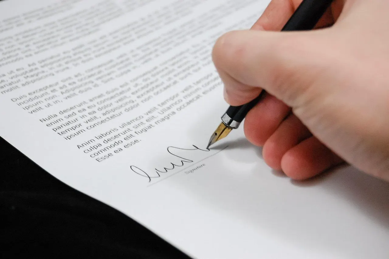 Hand mit Füllfederhalter unterschreibt ein Textdokument mit Unterschriftszeile.