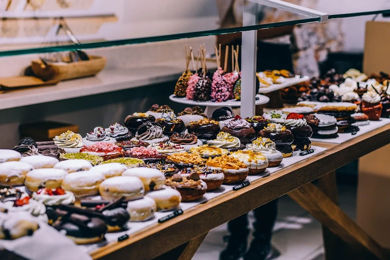 Theke mit zahlreichen glasierten Donuts und Gebäck, teils mit Streusel und Schokoladenglasur, auf Holzbrettern präsentiert.